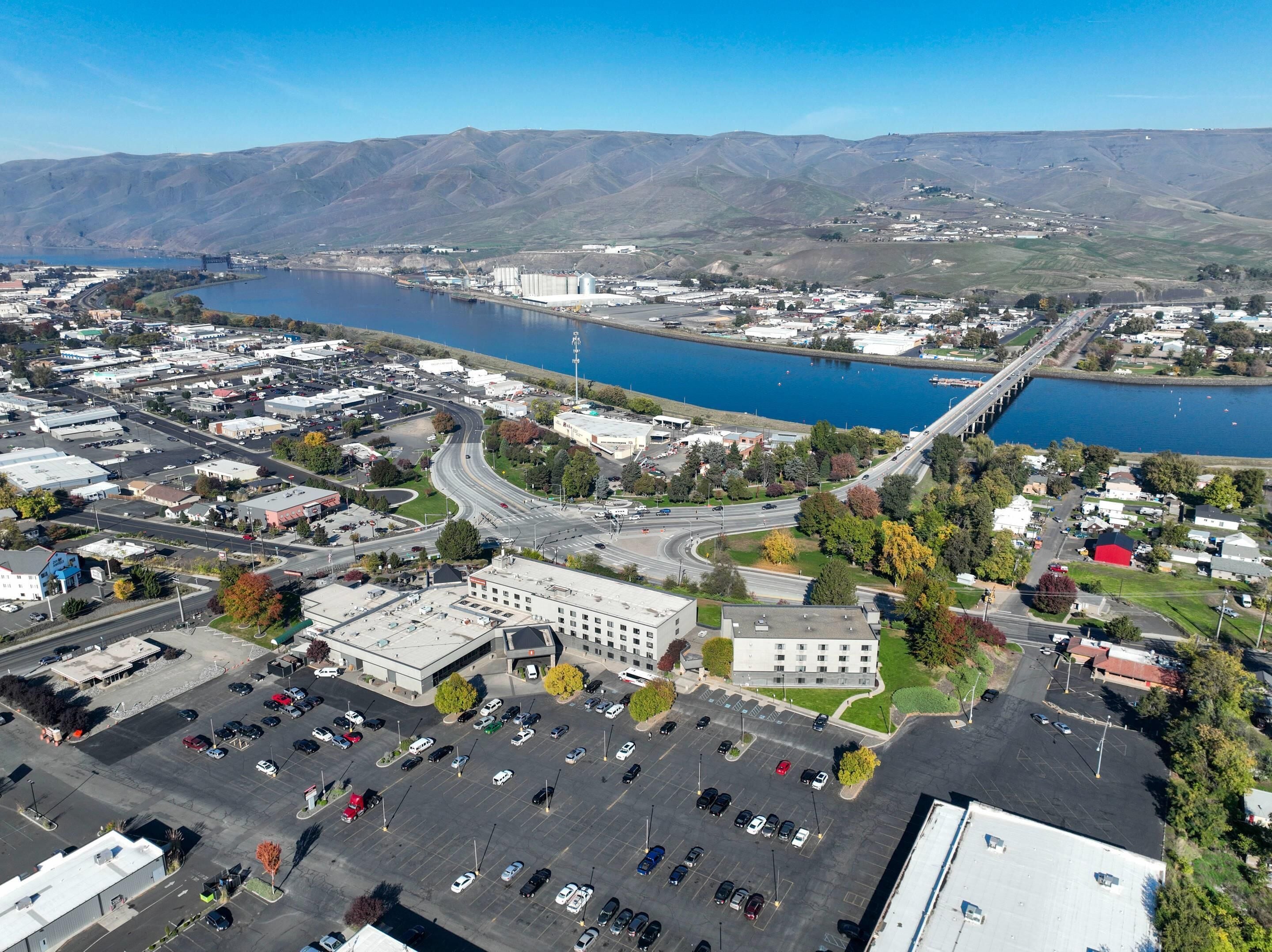 An aerial view of a town with a large parking lot, a bridge, and a body of water.