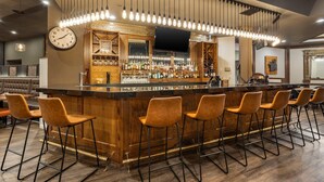 A bar area with a wooden counter, bar stools, a clock, and hanging light fixtures. - Hells Canyon Grand Hotel, an Ascend Collection Hotel (Lewiston)