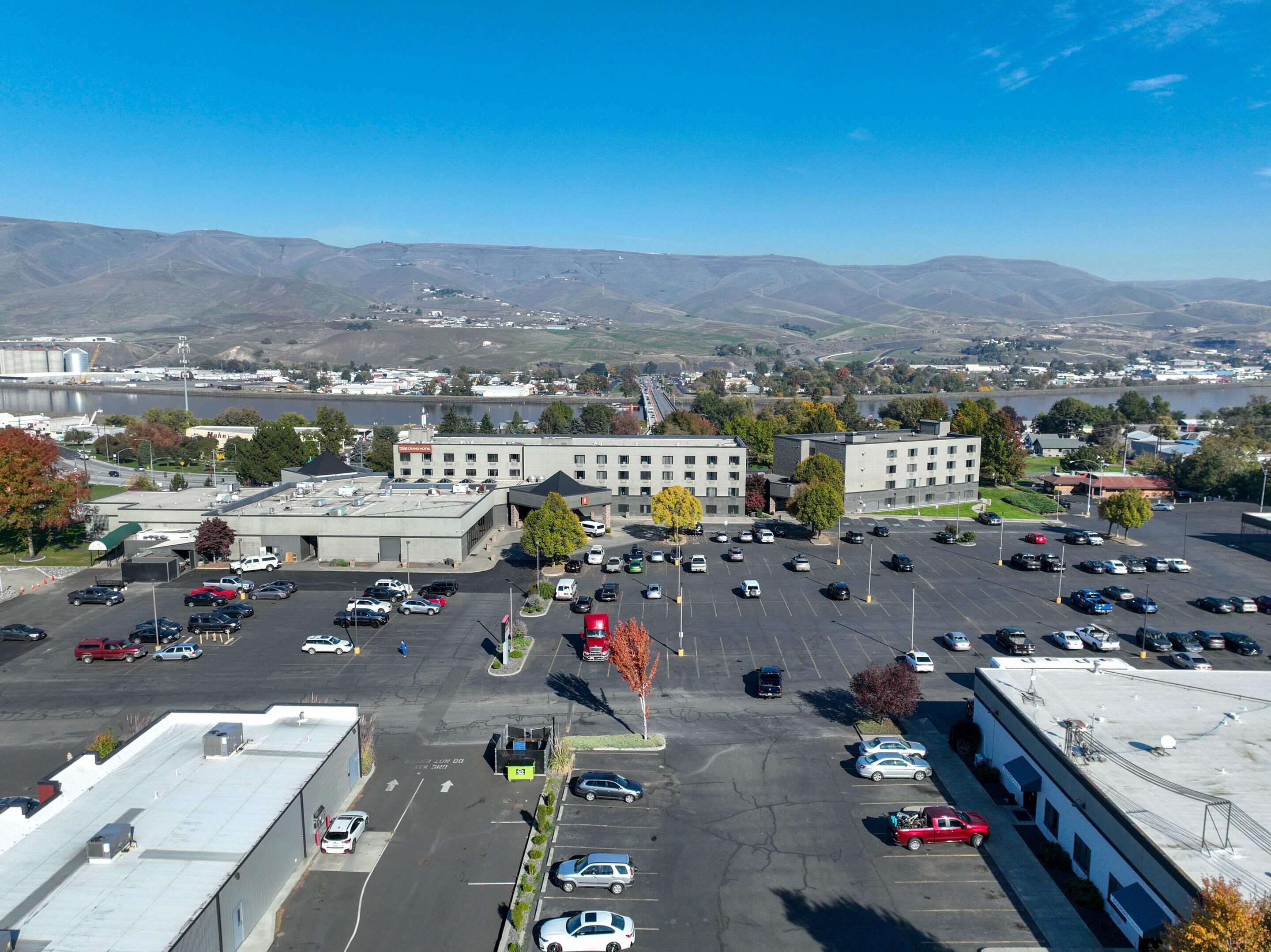 A parking lot with multiple cars, a building with a flat roof, and a mountainous landscape in the background.