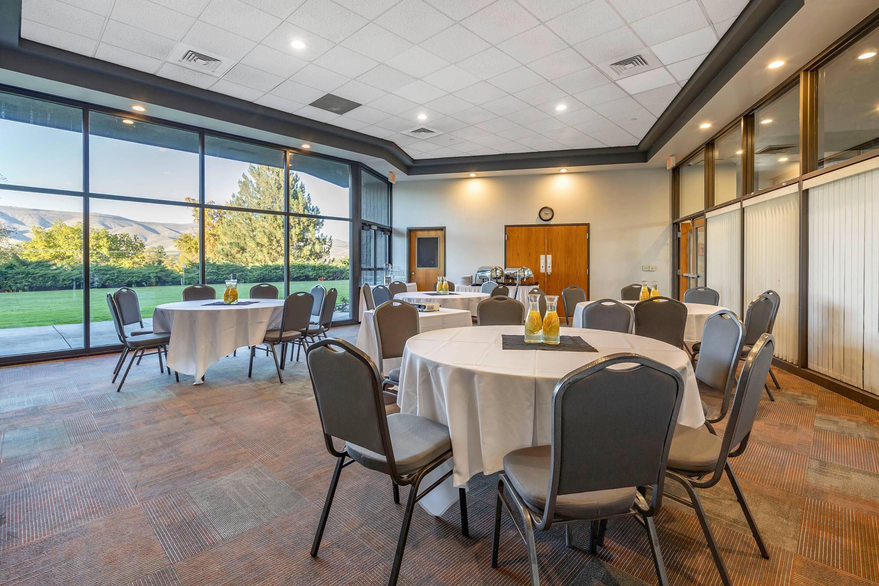 A conference room with round tables, chairs, and a large window offering a view of a green landscape.