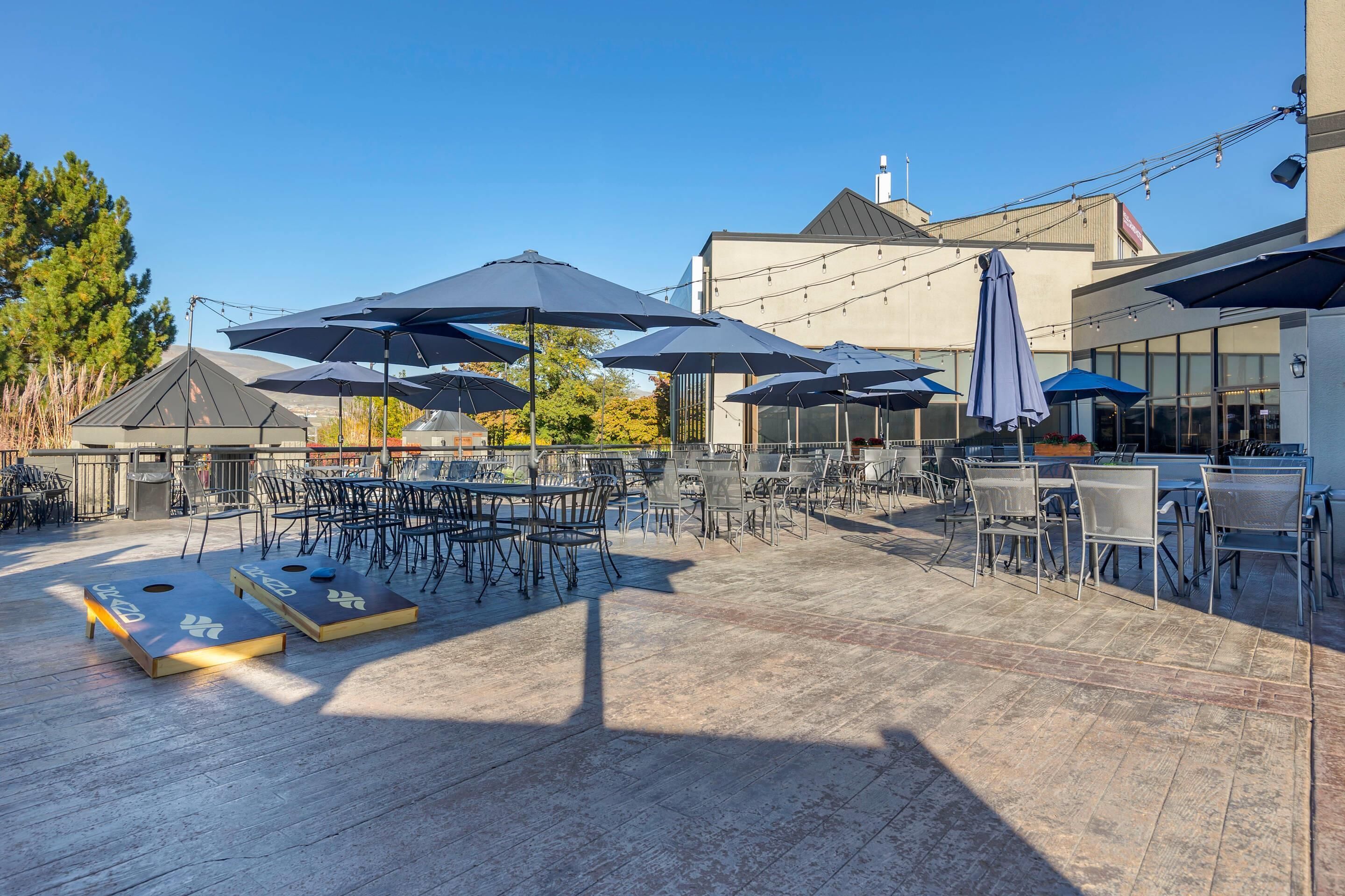 An outdoor patio with tables and chairs, umbrellas, and a wooden deck.
