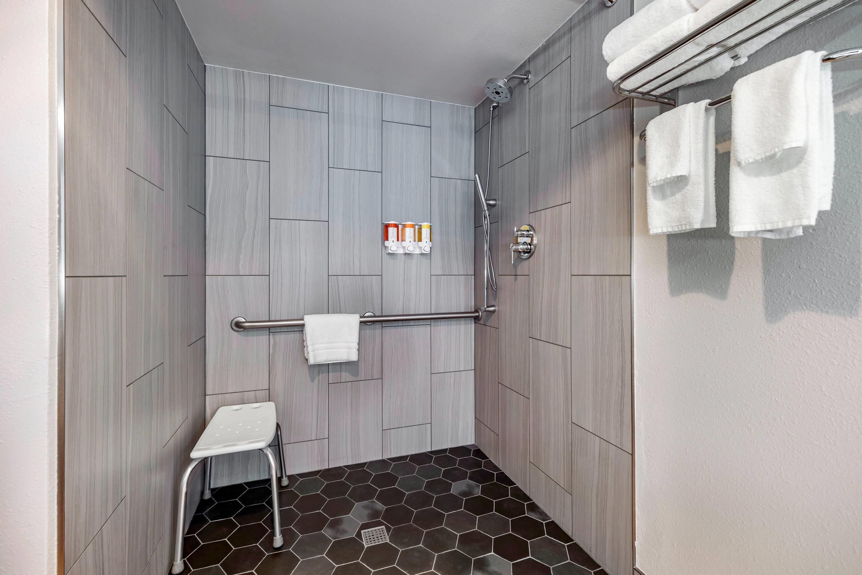 A modern shower area with a wooden wall, a white towel rack, a small white stool, and a shower control panel.