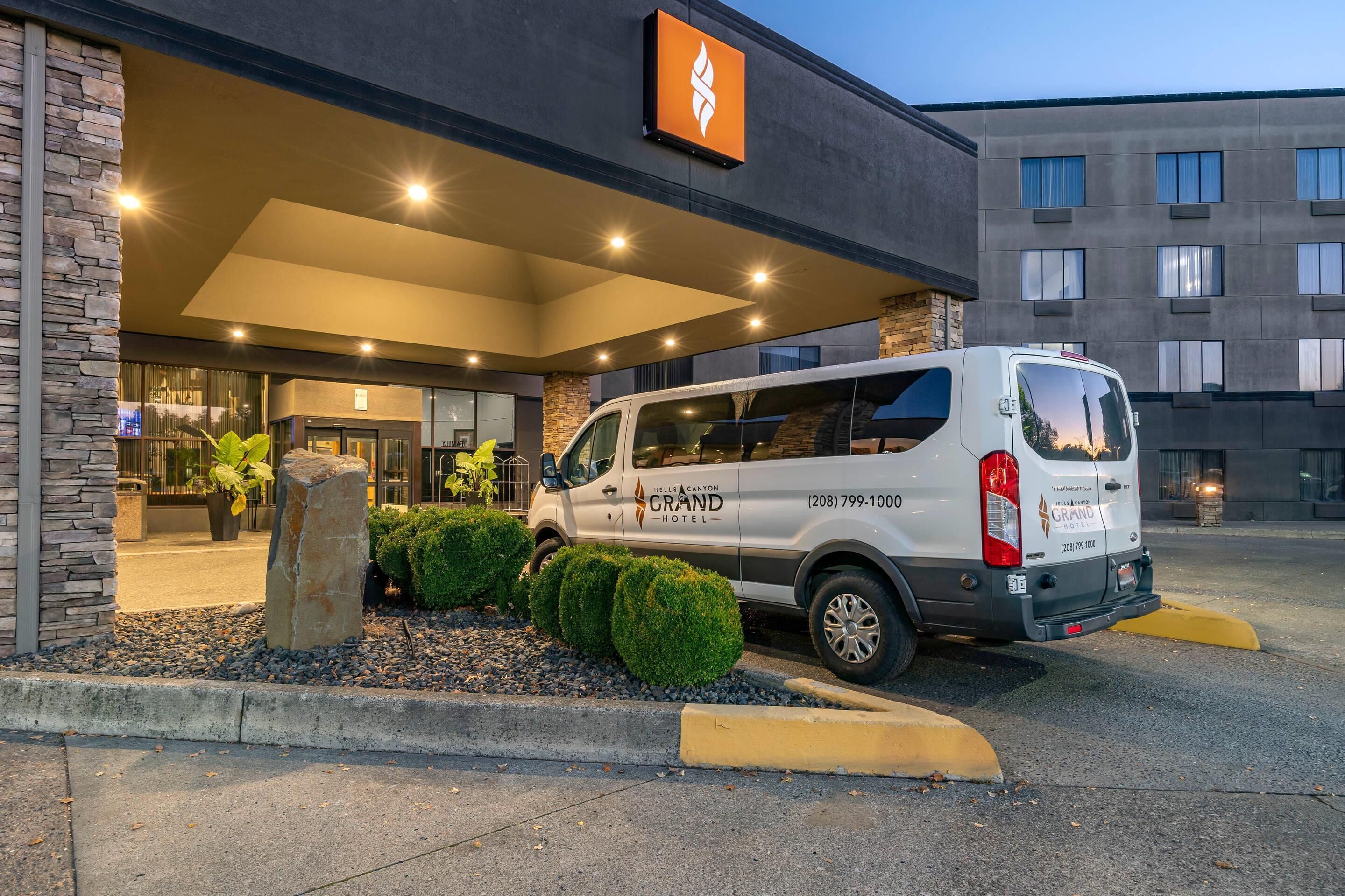 Un furgone bianco parcheggiato di fronte a un hotel con facciata in pietra e un cartello sopra l'ingresso.