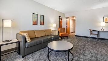 A hotel room with a gray sofa, a round coffee table, a side table, a chair, and two wall-mounted lamps.