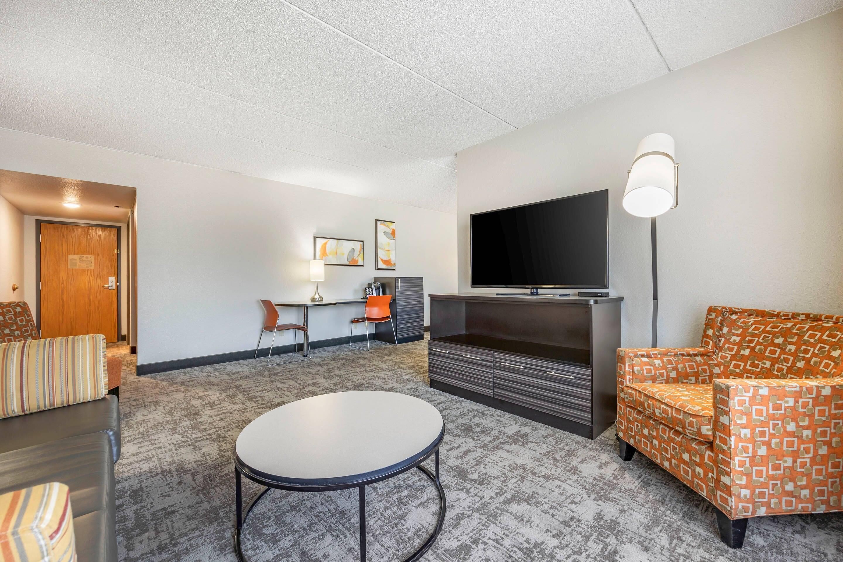 A modern living room with a flat-screen TV, a sofa, a patterned armchair, a coffee table, and a desk with a chair.
