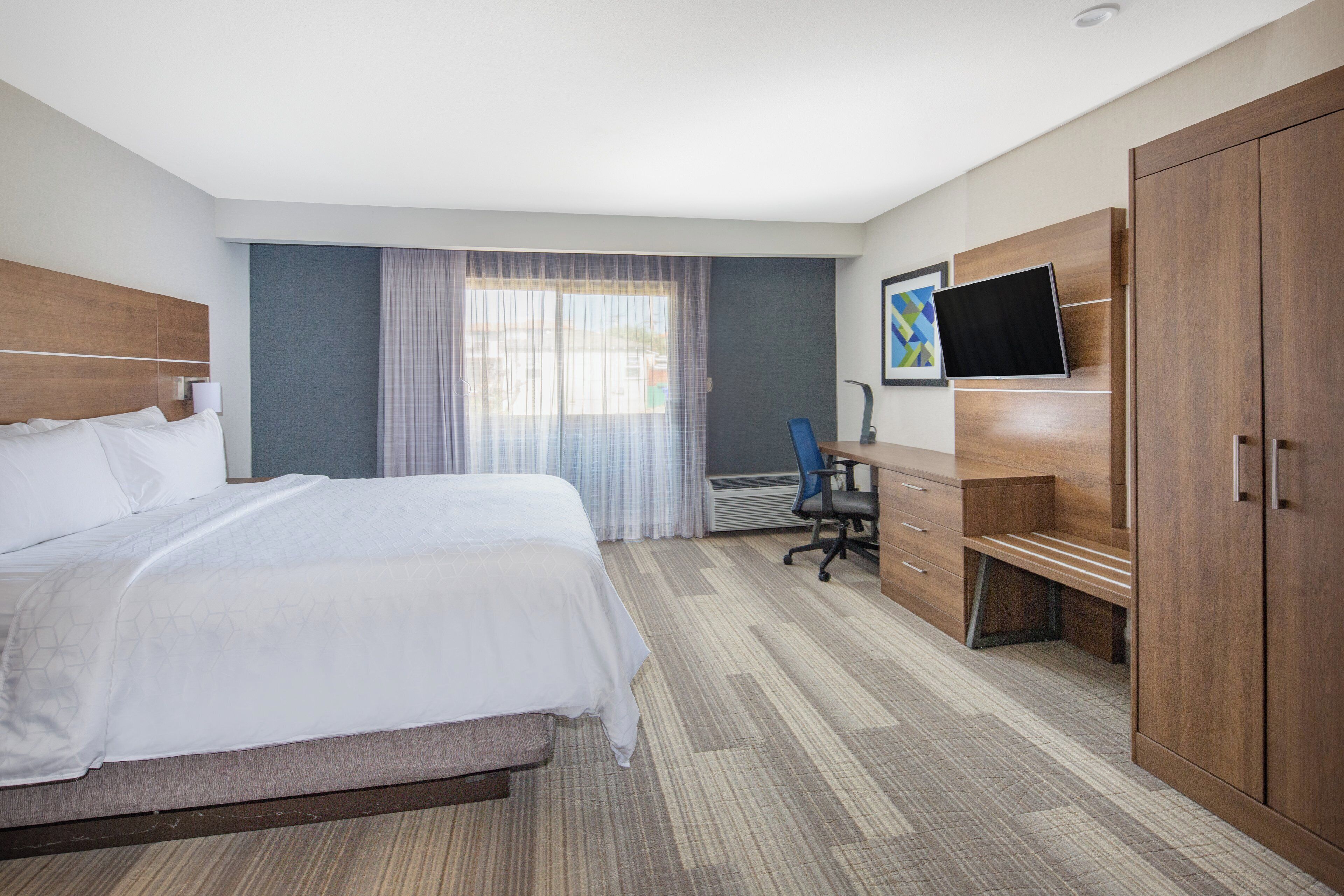 A hotel room with a bed, a desk, a chair, a TV, and a wardrobe.