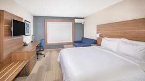 Une chambre d’hôtel avec un grand lit, un bureau avec une chaise, une télévision et une fenêtre avec des stores.