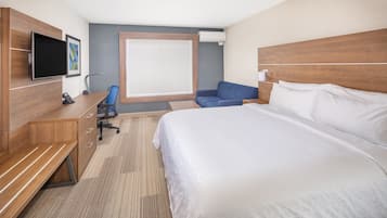 Une chambre d’hôtel avec un grand lit, un bureau avec une chaise, une télévision et une fenêtre avec des stores.
