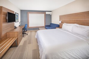 Une chambre d’hôtel avec un grand lit, un bureau avec une chaise, une télévision et une fenêtre avec des stores.