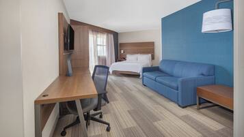 A hotel room with a bed, a blue sofa, a desk with a chair, and a television.