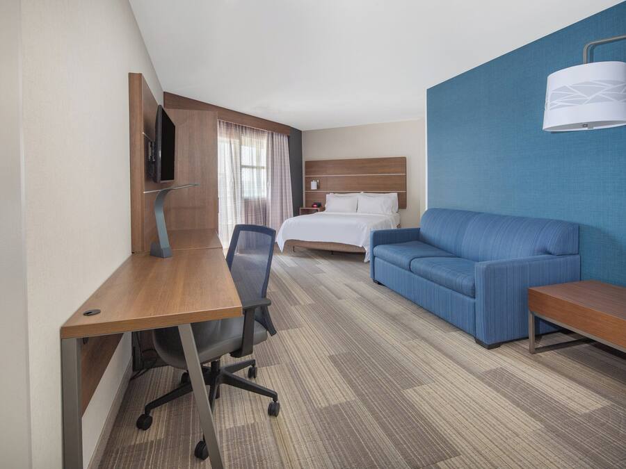 A hotel room with a bed, a blue sofa, a desk with a chair, and a television.