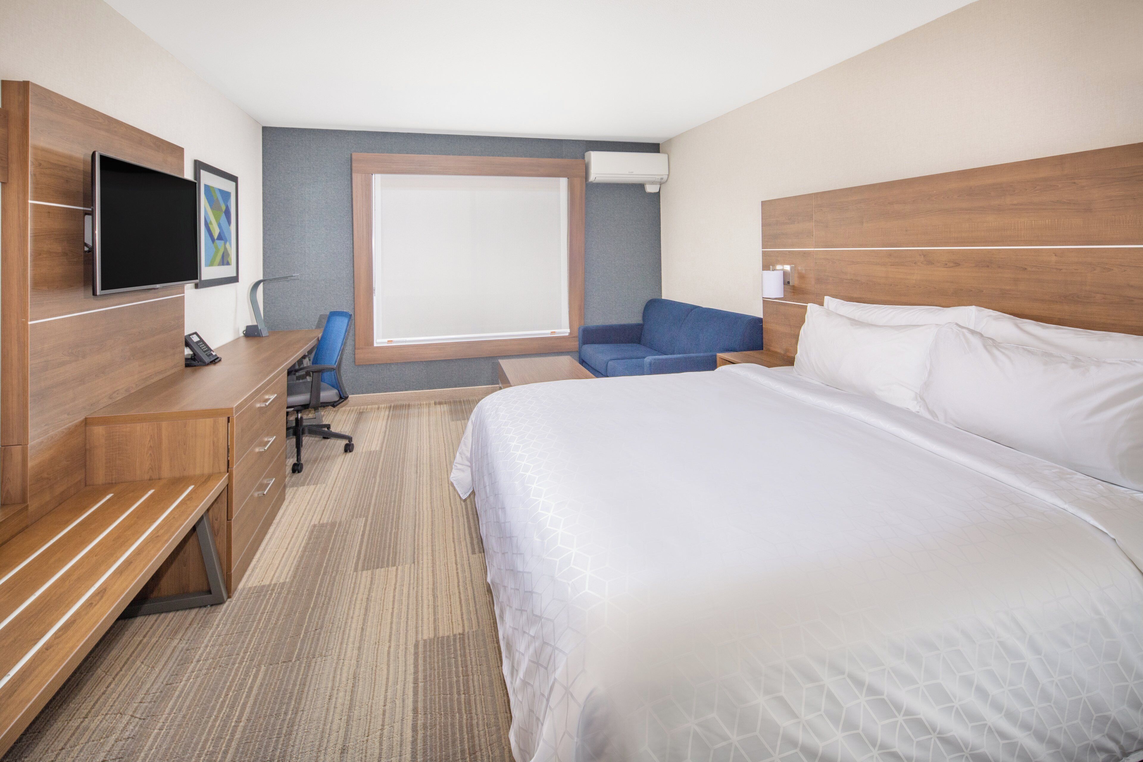 Una habitación de hotel con una cama grande, un escritorio con silla, un televisor y una ventana con vistas.