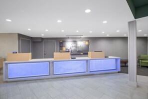 Ein Empfangsbereich im modernen Stil mit einer Rezeption, beleuchteten Paneelen, einem digitalen Display und einer Theke mit dem Schild Holiday Inn Express.