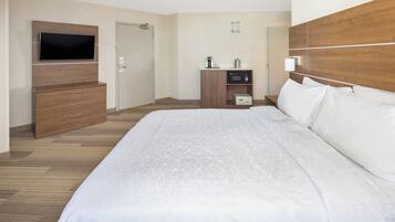 A hotel room with a large bed, a television mounted on the wall, a wooden cabinet, and a microwave on a shelf.
