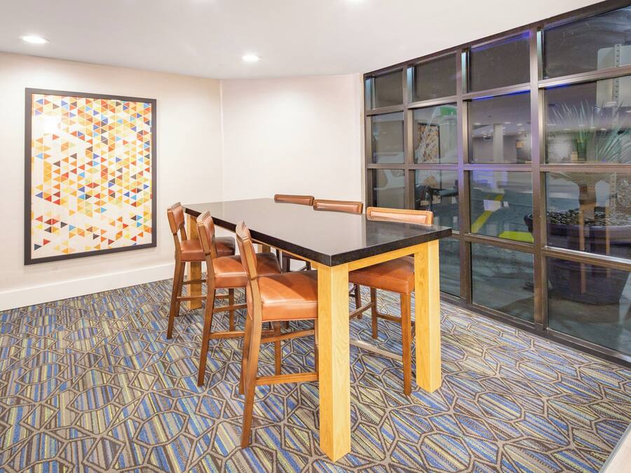 A conference room with a long table, chairs, a patterned carpet, and a large window with reflections.