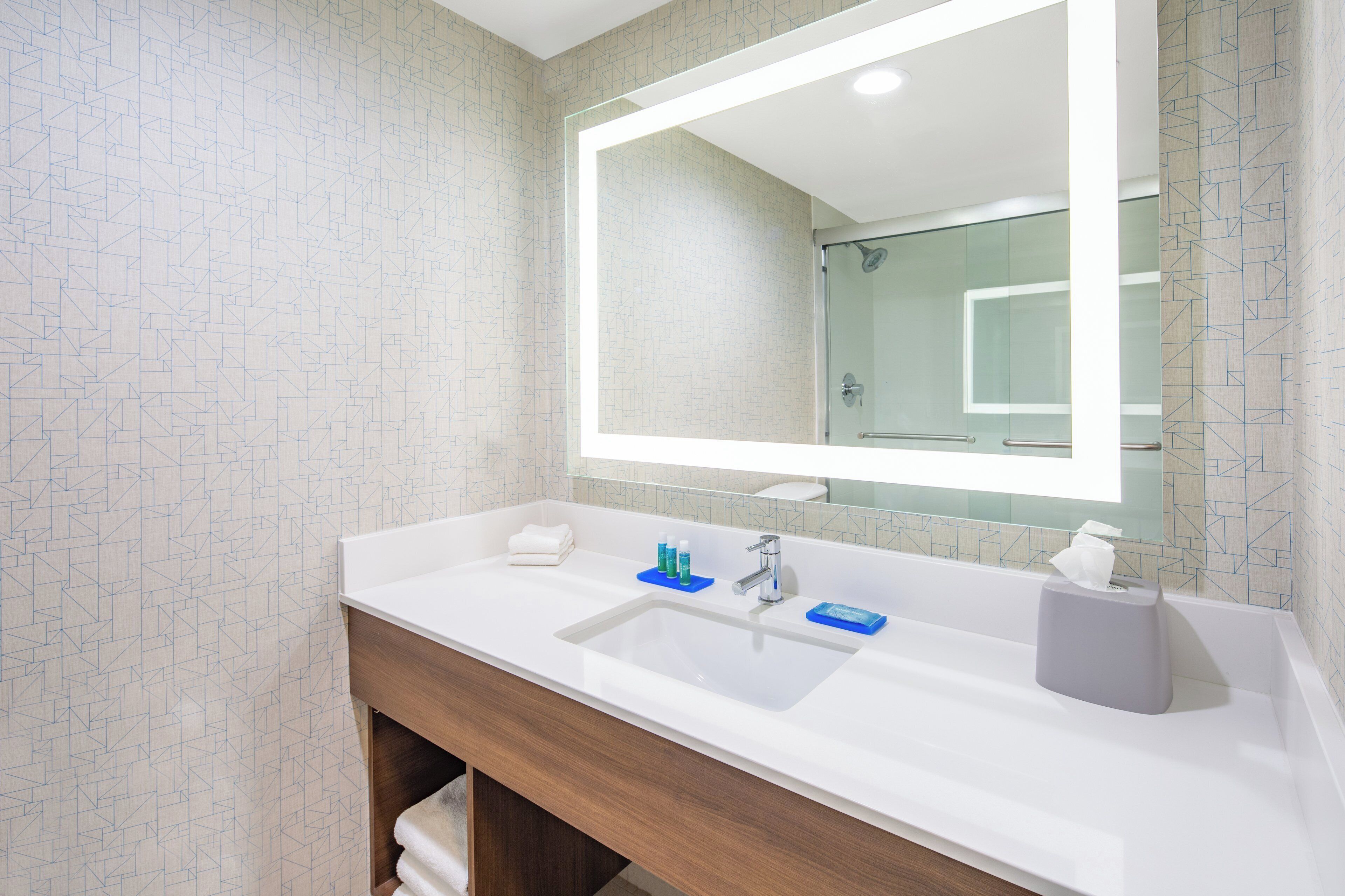 Un baño moderno con un espejo grande, lavamanos blanco y tocador de madera.