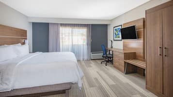 A hotel room with a bed, a desk, a chair, a TV, and a wardrobe.