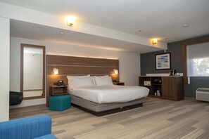 A modern hotel room with a large bed, bedside tables, a desk, a chair, a mirror, and a window.