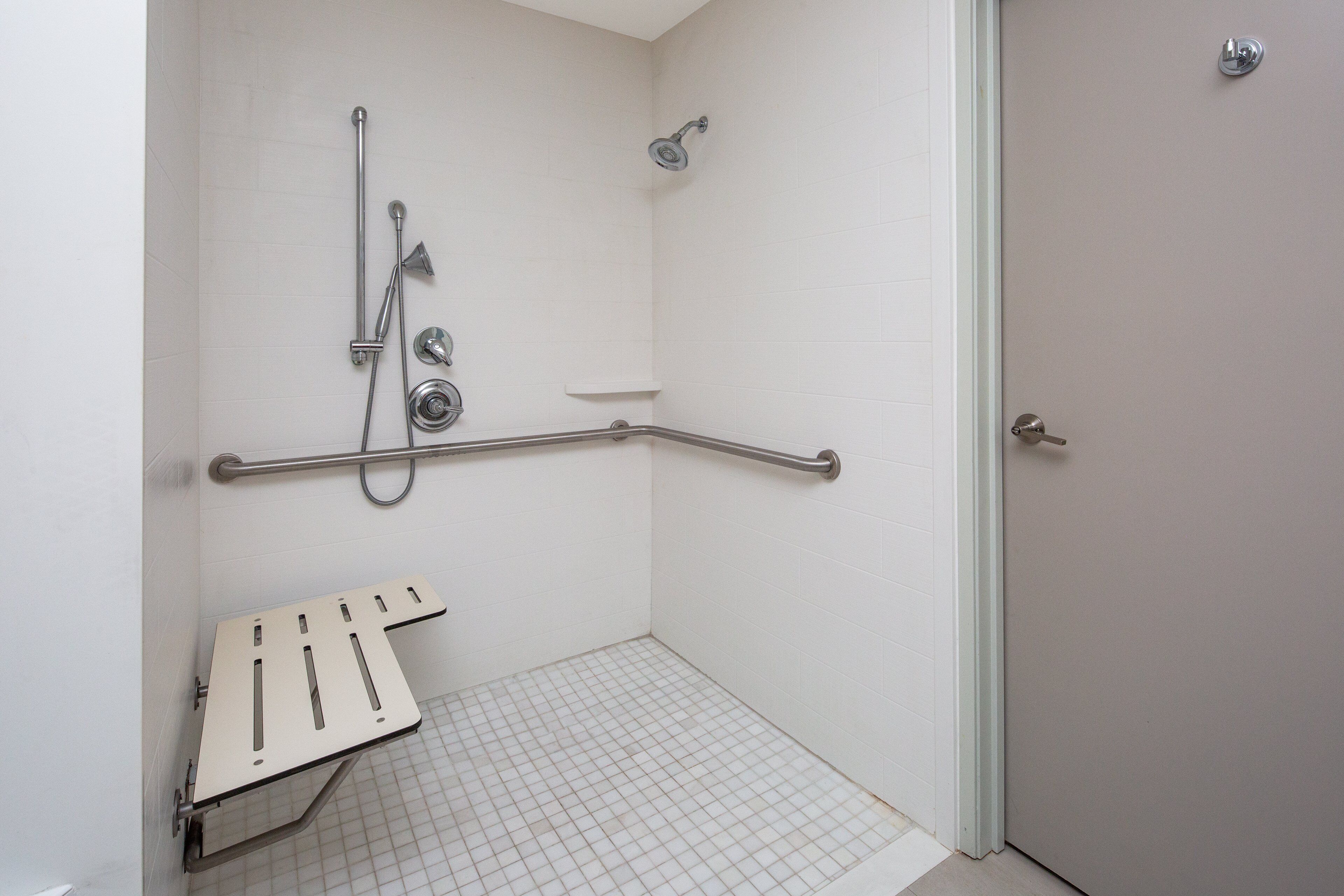 A bathroom with a shower, grab bars, and a wheelchair-accessible bench.
