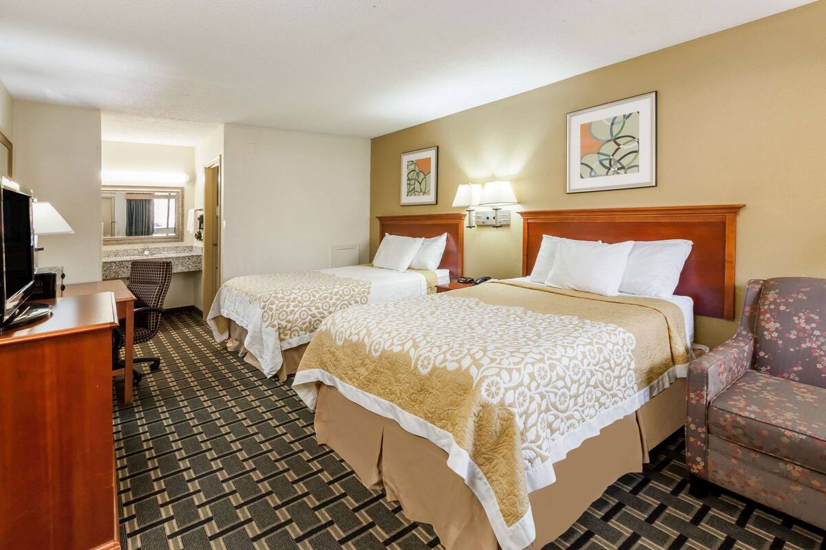 A hotel room with two beds, a desk, a chair, a television, and artwork on the walls.