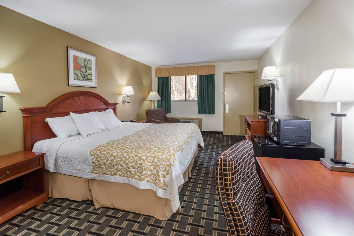 A hotel room with a bed, a desk, a TV, and a chair.