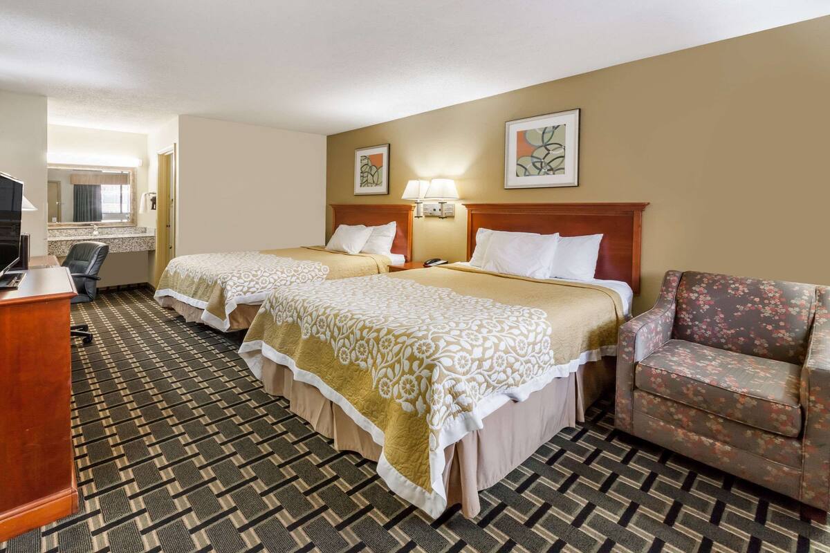 A hotel room with two beds, a desk, a chair, and a television.