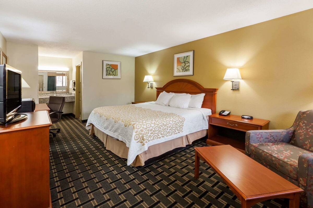 A hotel room with a bed, a desk, a chair, a TV, and two wall-mounted lamps.