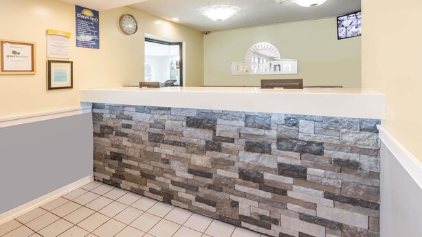 A reception area with a stone accent wall, a clock, and a sign for Days Inn. - Days Inn by Wyndham Kent - Akron (Kent)