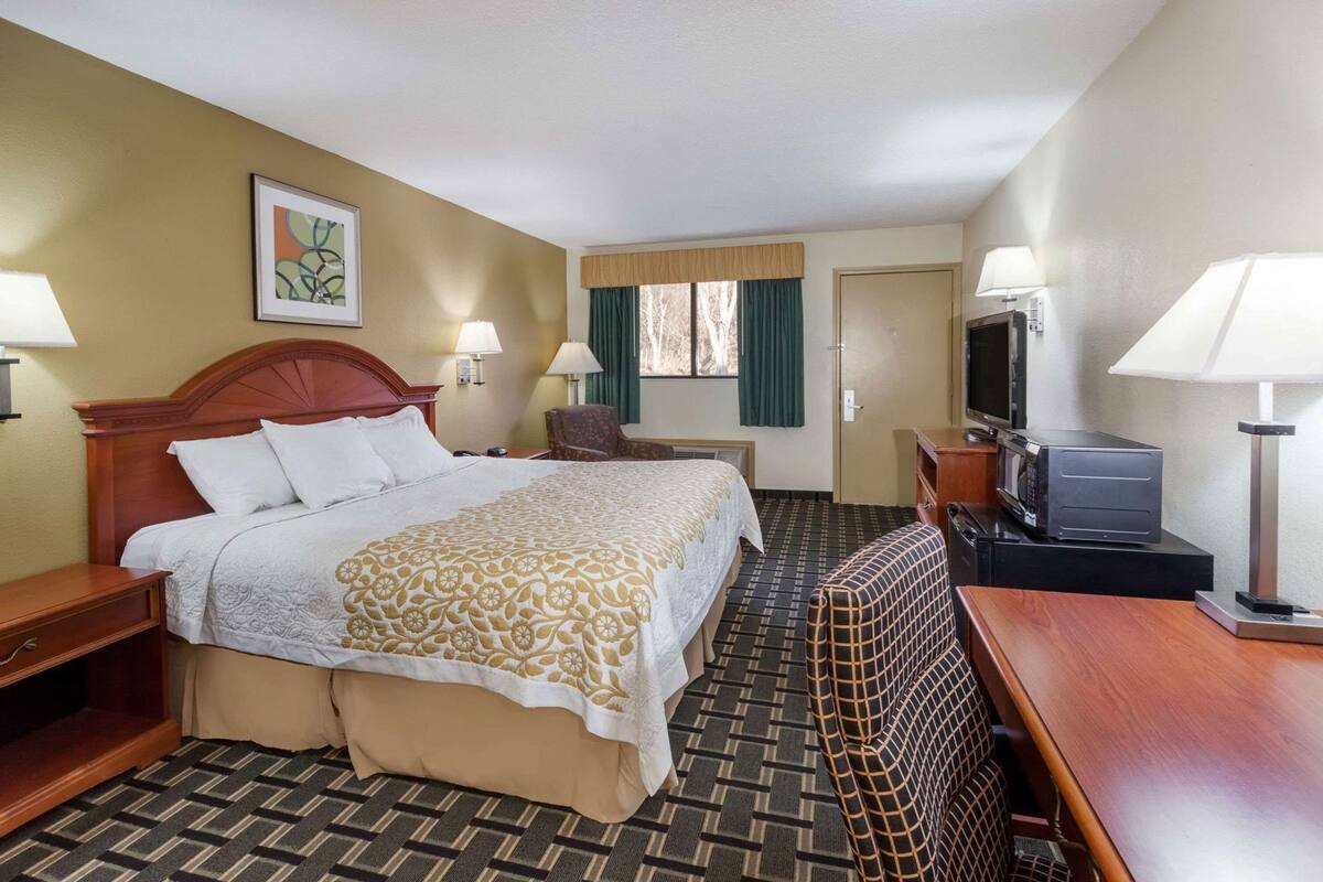 A hotel room with a bed, a desk, a television, and a chair.