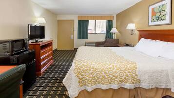 A hotel room with a bed, a desk with a television, a microwave, a dresser, and a chair.