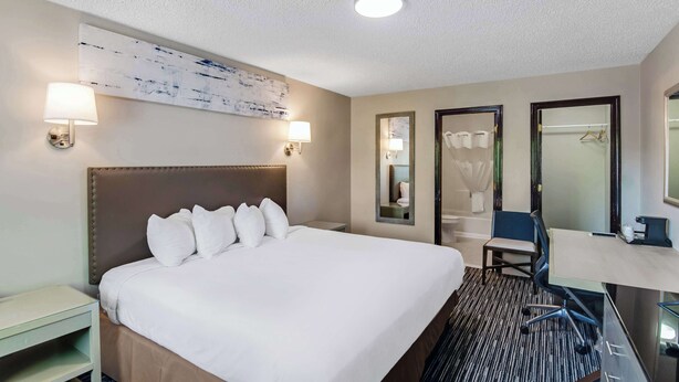 Ein Hotelzimmer mit einem großen Bett, Nachttischlampen, einem Schreibtisch mit Stuhl, einem Spiegel und einem Kleiderständer.