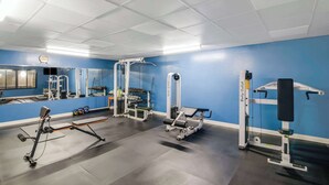 Ein Fitnessstudio mit unterschiedlichen Trainingsgeräten, einem Spiegel und einer blauen Wand.