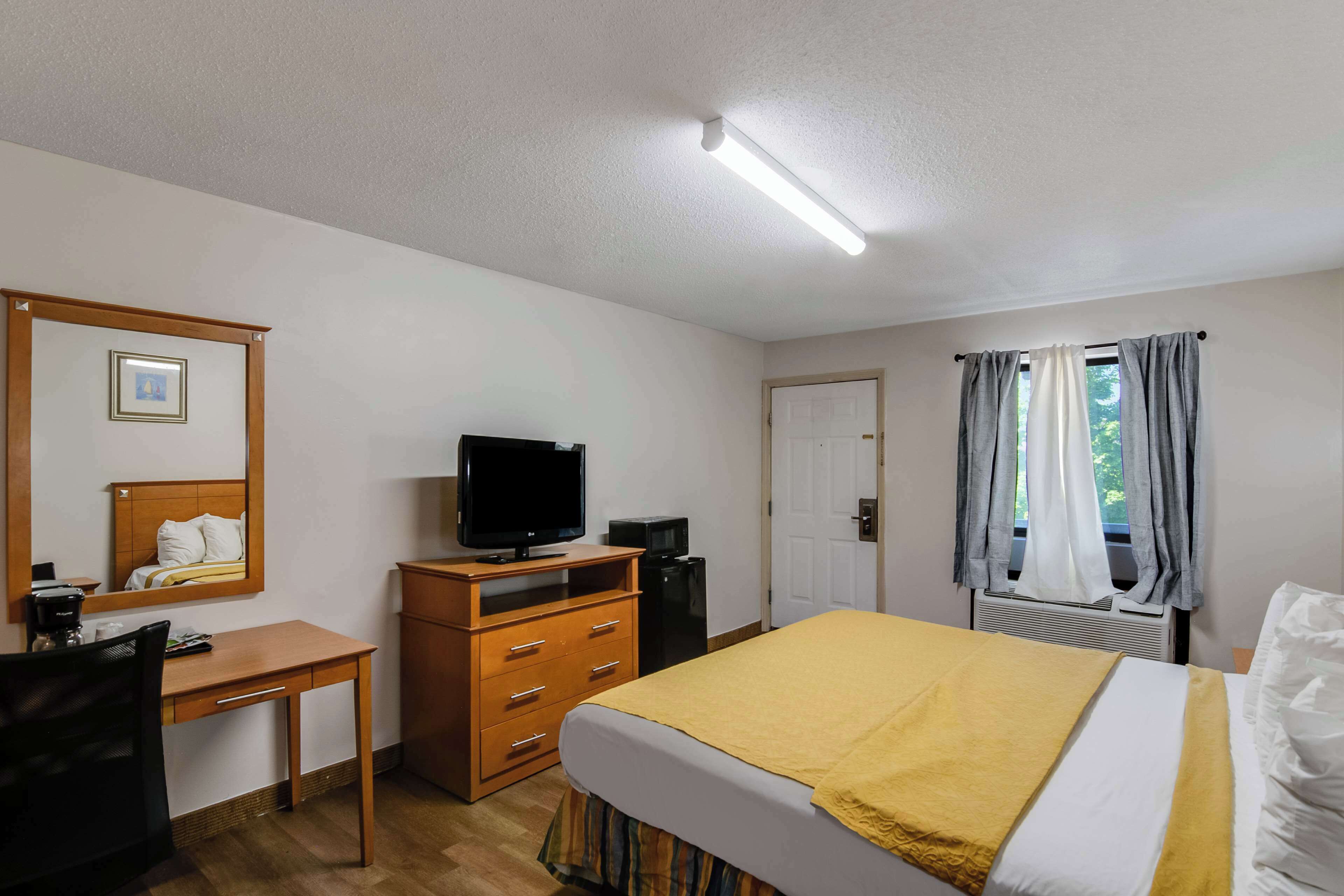 A hotel room with a bed, a desk, a television, and a window with curtains.