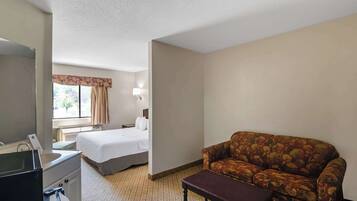 A hotel room with a bed, a sofa, a small table, a desk with a telephone, and a window with curtains.