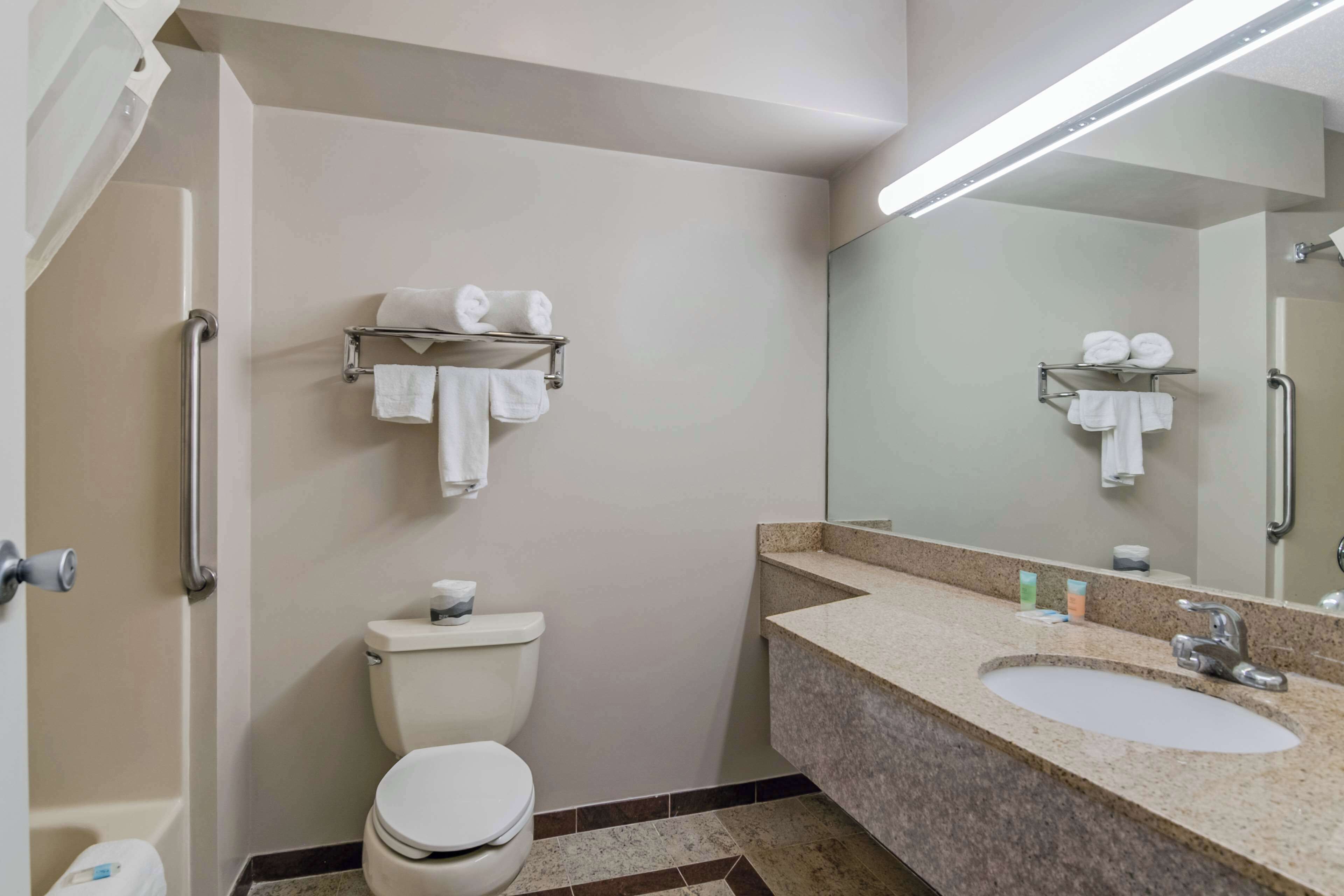 Un baño con inodoro, lavamanos y barras de apoyo.