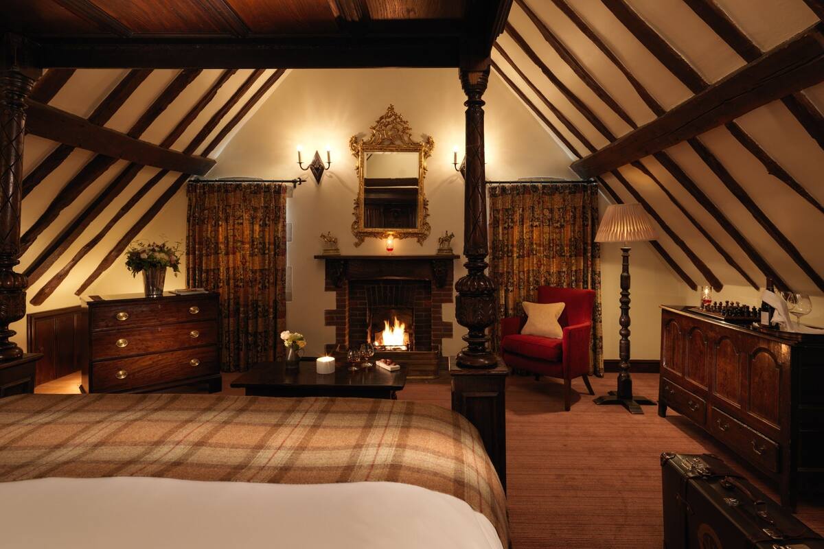 A traditional room with a fireplace, a bed, a red armchair, and a chessboard.