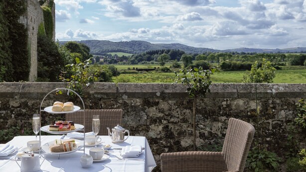 Una mesa preparada para el té, con vistas a ondulantes colinas y un castillo al fondo.