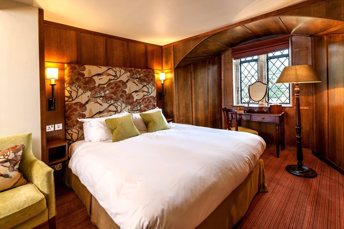 A hotel room with a large bed, wooden paneling, a desk with a lamp, and a window with a view.