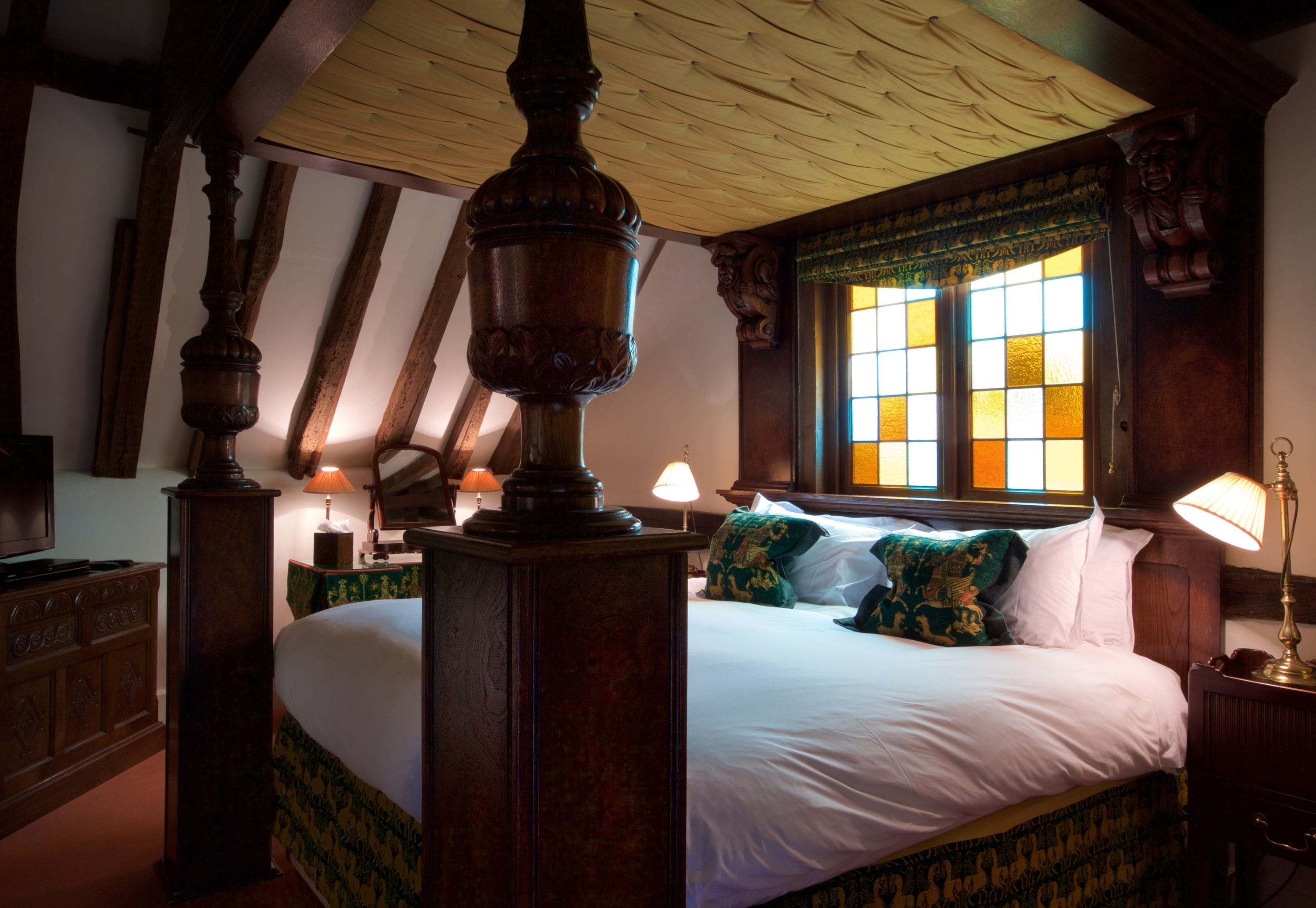 Une chambre traditionnelle avec un grand lit, des poutres apparentes et une fenêtre ornée de vitraux.
