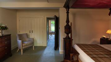 A bedroom with a four-poster bed, a chair, a dresser, and a nightstand with a lamp.