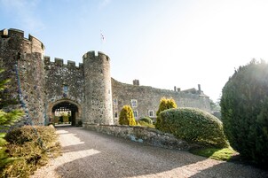 Un castillo de piedra histórico con un arco central, rodeado de setos bien cuidados y un camino de grava que lleva a la entrada.