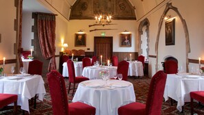 Un comedor con mesas redondas, sillas tapizadas en rojo, candelabros y cuadros enmarcados en las paredes.