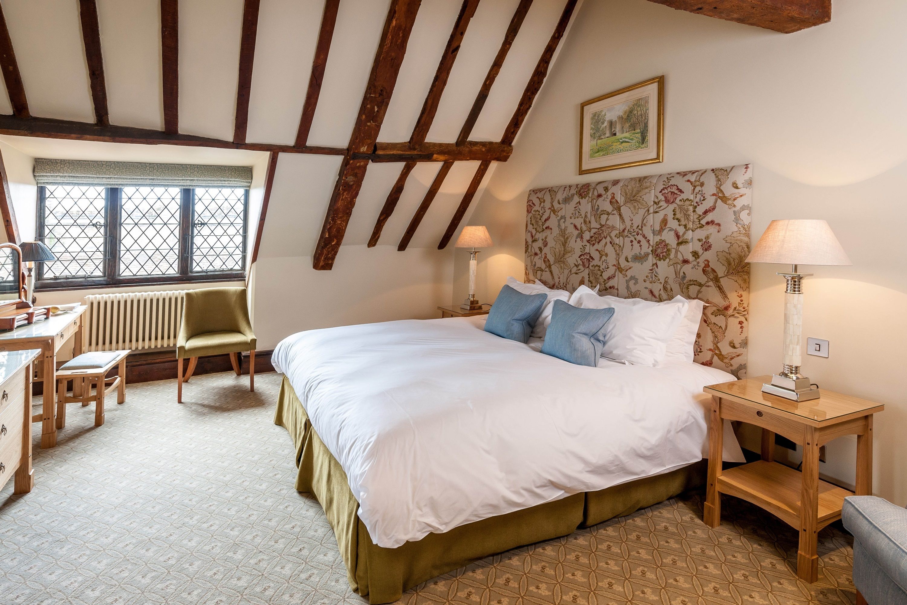 A bedroom with a large bed, wooden headboard, two bedside tables with lamps, a desk, and a chair.