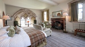 Un dormitorio amplio con una cama grande, una chimenea y vistas al exterior a través de ventanas de arco.