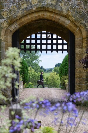 A stone archway with a lattice design, leading to a pathway surrounded by greenery.