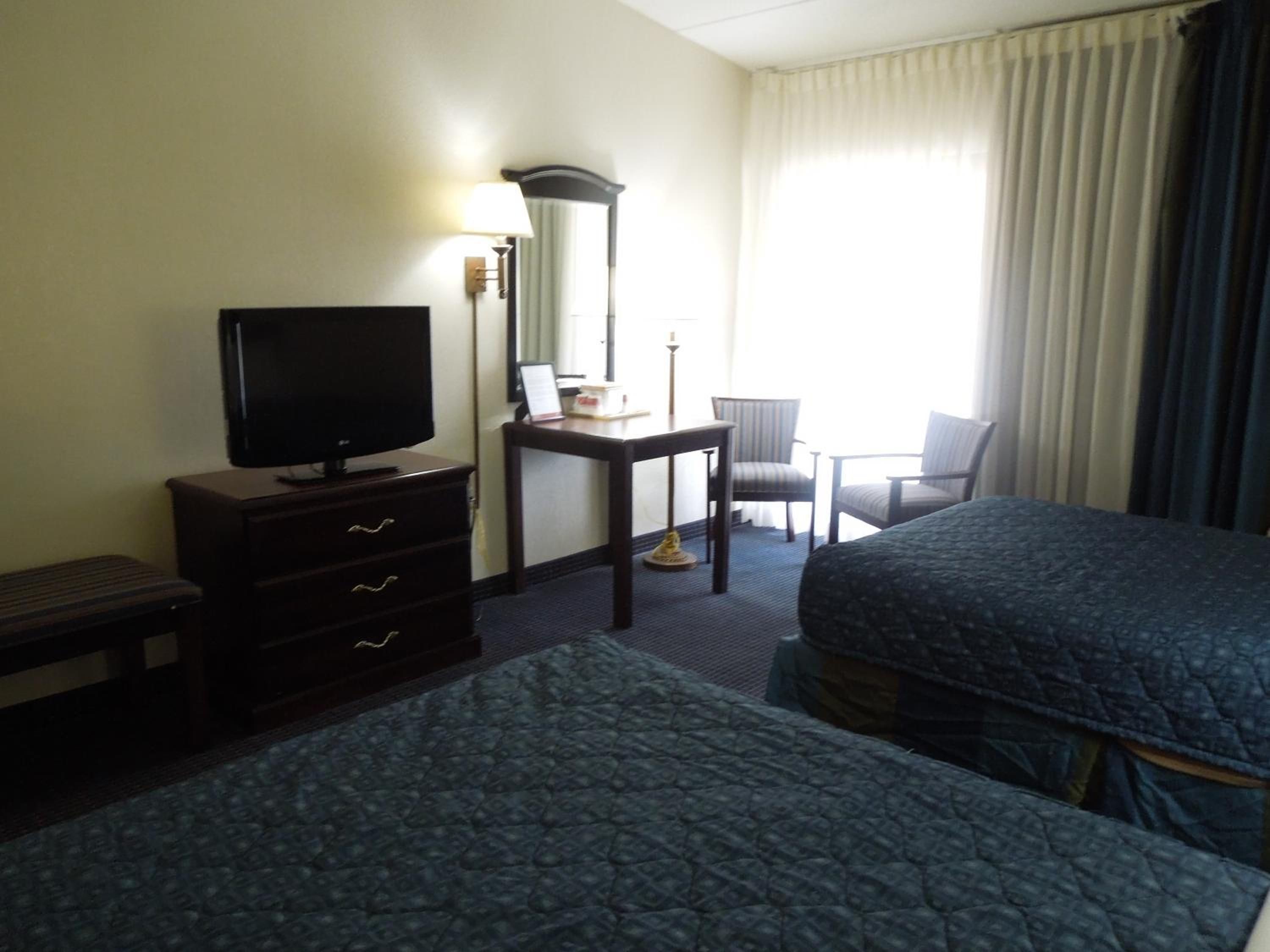 Habitación de hotel con dos camas, un escritorio con silla, televisor y ventana con cortinas.