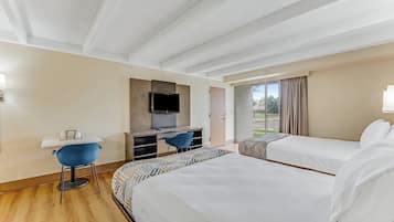 Habitación de hotel con dos camas, un escritorio con silla, televisión y un amplio ventanal con cortinas.