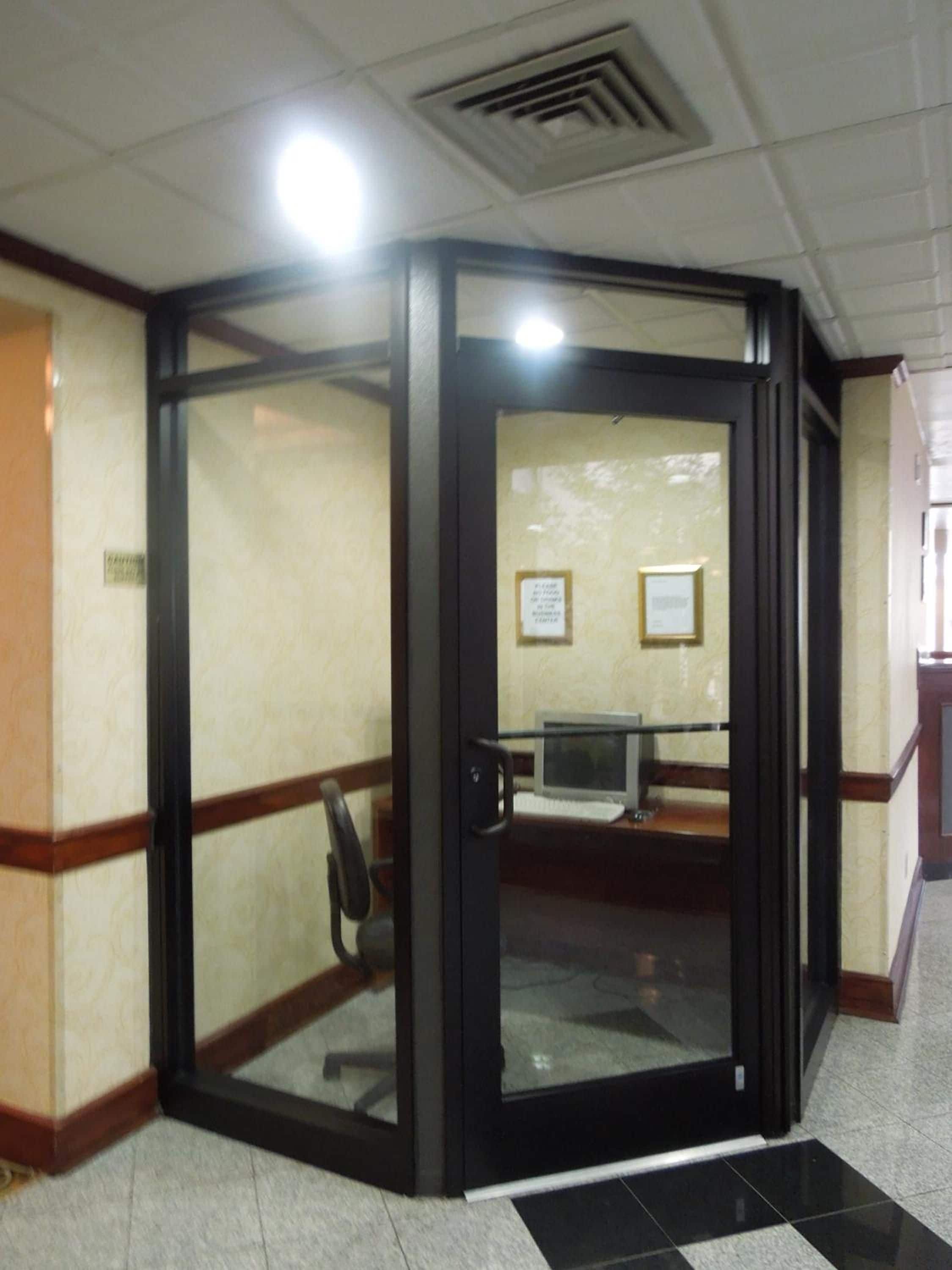 Una puerta giratoria con un panel de vidrio, un escritorio con un ordenador y un certificado enmarcado en la pared.