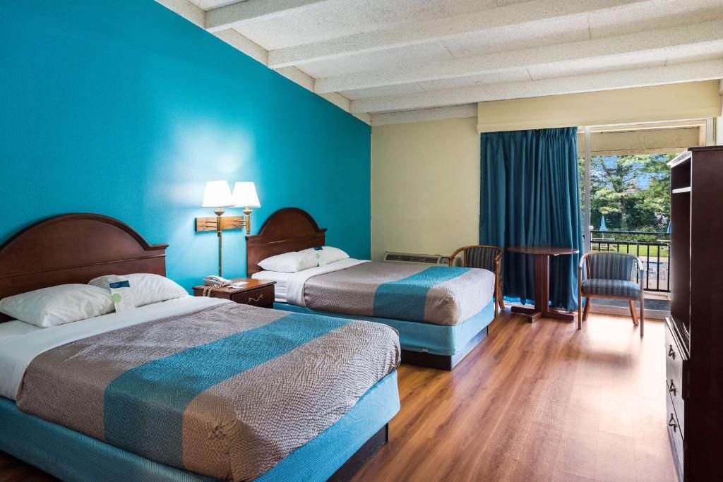 A hotel room with two beds, a desk, a chair, and a balcony.