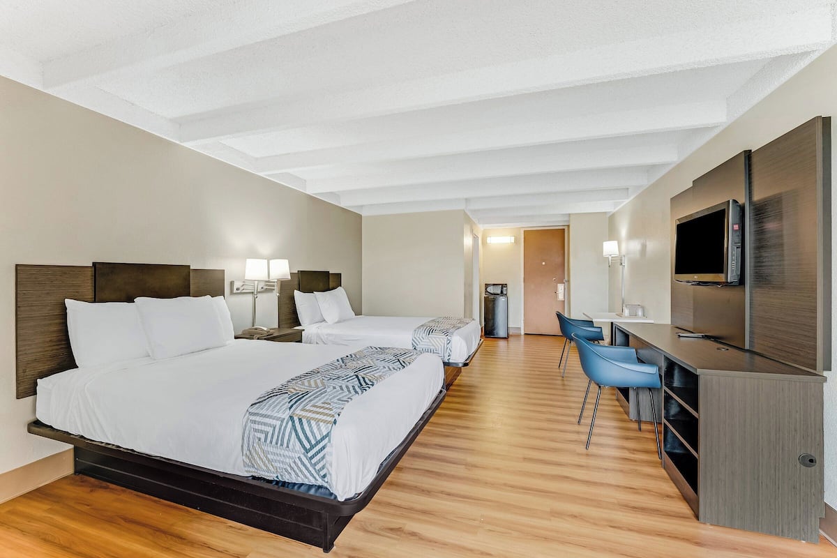 A hotel room with two beds, a desk with chairs, a TV, and a trash can.